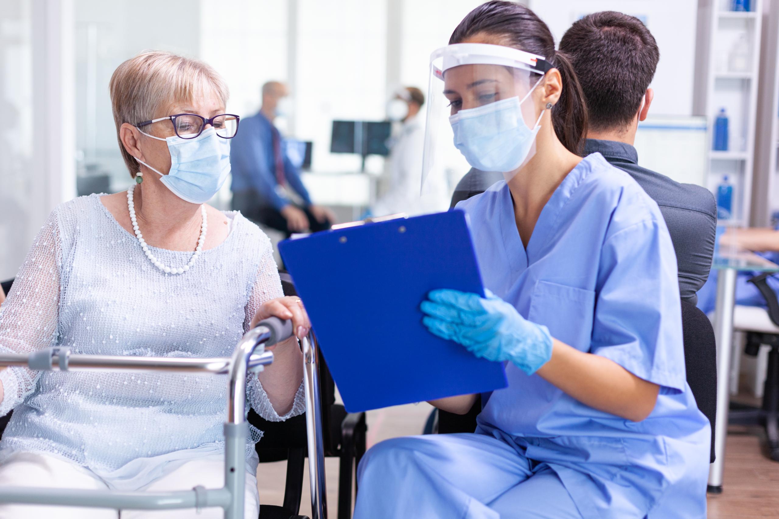 disabled-senior-woman-having-discussion-with-medical-specialist-about-treatment-hospital-hallway-wearing-face-mask-against-coronavirus-scaled