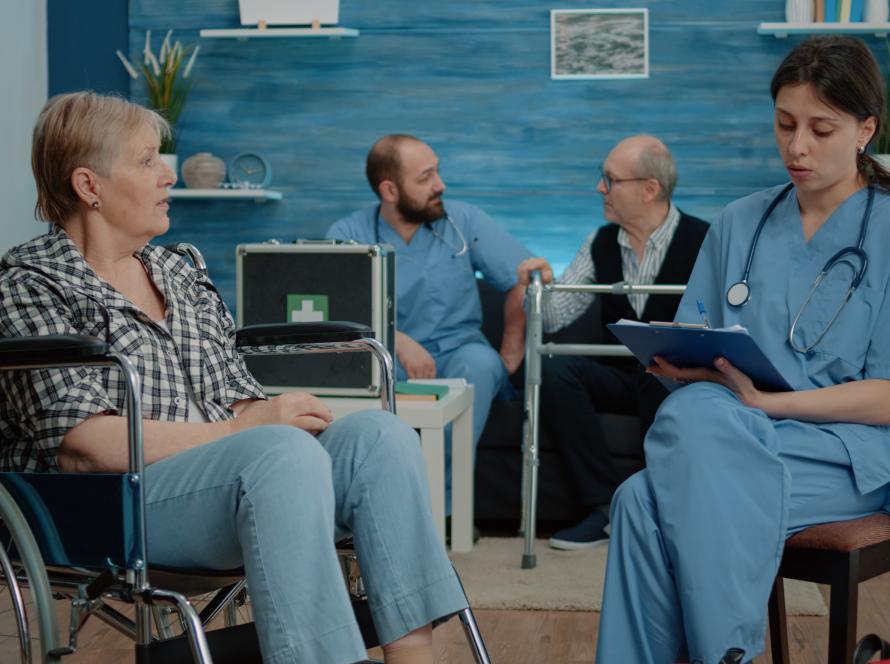 retired-woman-with-disability-talking-nurse-medical-checkup-nursing-home-healthcare-assistant-consulting-elderly-patient-sitting-wheelchair-support-assistance.